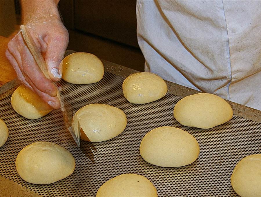 Mehrere Brötchenteiglinge werden von einem Bäcker bestrichen